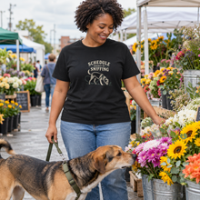 Load image into Gallery viewer, Illustrative woman wearing the Black Schedule Subject to Sniffing T-shirt at a flower market with a mixed-breed dog
