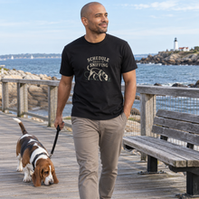 Load image into Gallery viewer, Illustrative man wearing the Black Schedule Subject to Sniffing T-shirt on a boardwalk with a basset hound

